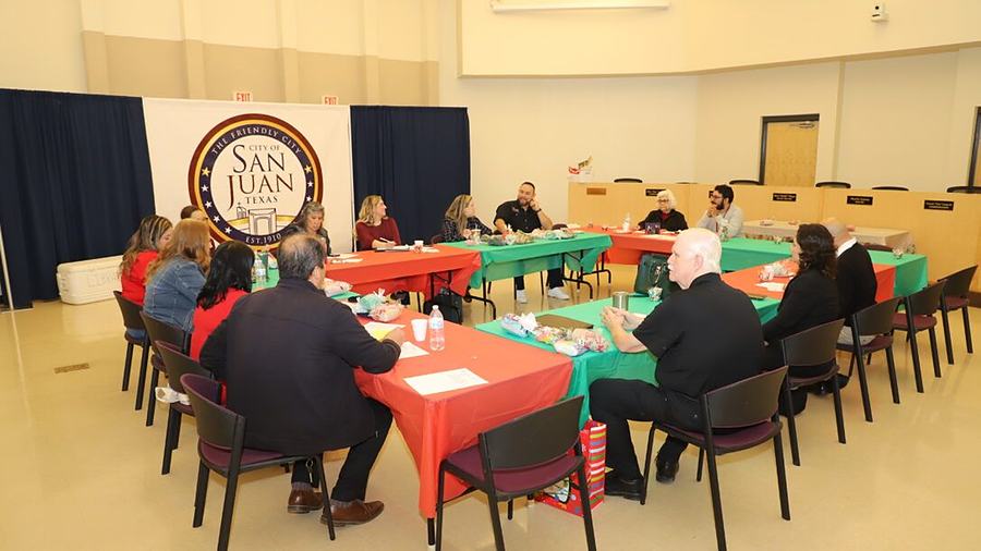 City staff seated around tables pushed into a square in a municipal meeting room, the city's “The Friendly City” banner on the wall behind them.