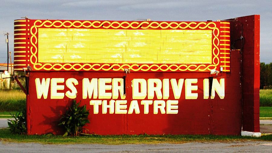 The Wes-Mer Drive-In sign, red with a border of round bulbs, standing over the grass.