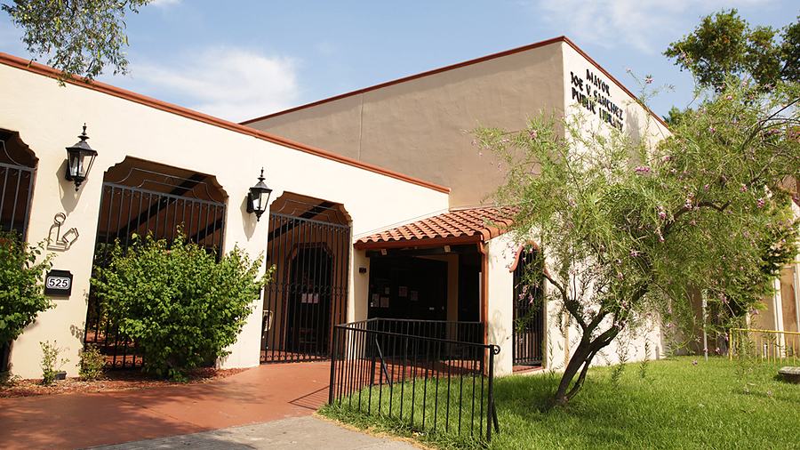 The Mayor Joe V. Sanchez Public Library, a low tile-roofed building behind trees.