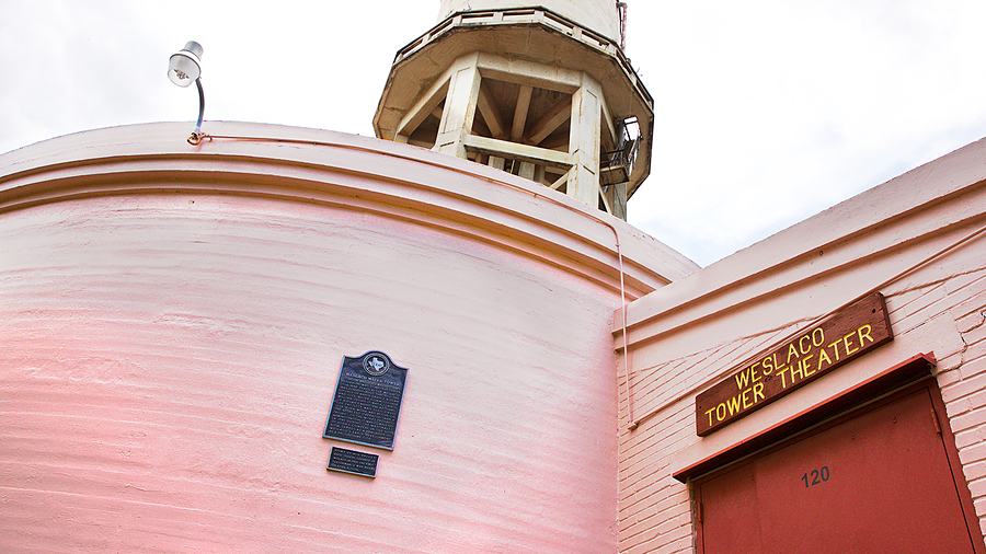 The Tower Theater in downtown Weslaco, its pink facade and lit sign against a blue sky.