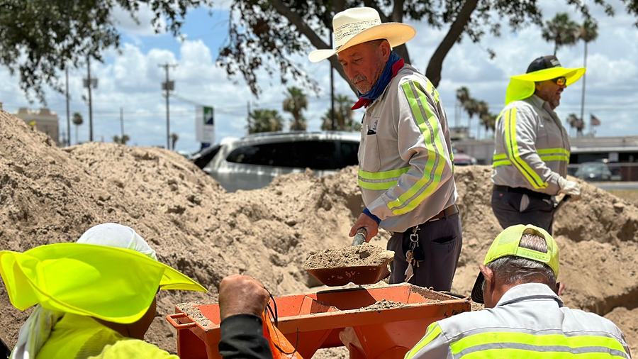 A City of Weslaco crew in hard hats and high-visibility vests working in an open trench.